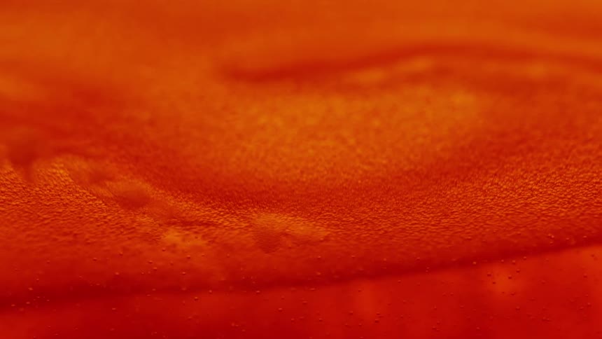 An extreme closeup shot details the swirling currents of a golden amber liquid filled with rising bubbles and topped with a shifting layer of thick foam