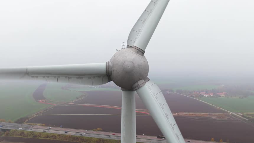 Close up view of a wind turbine spinning as traffic moves on the street below