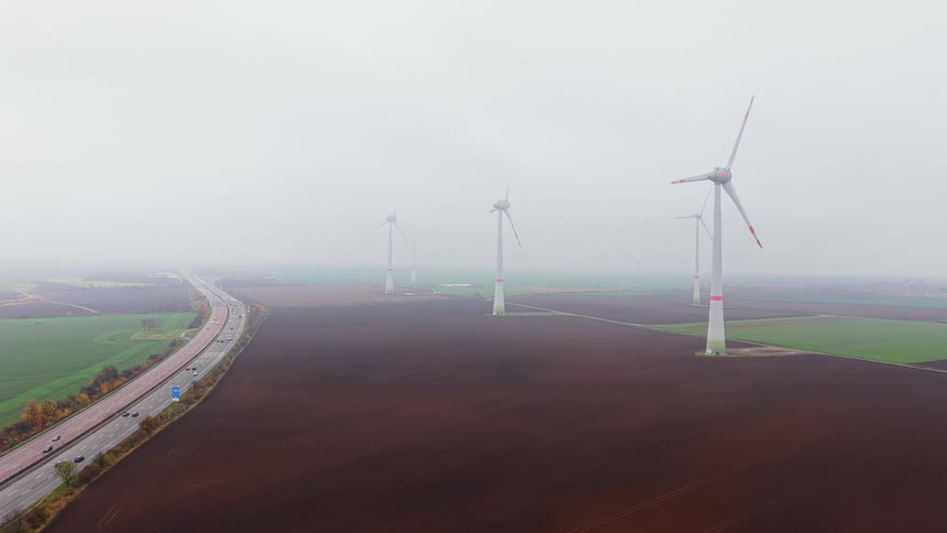 Turbines spin on a wind farm as traffic moves on the highway
