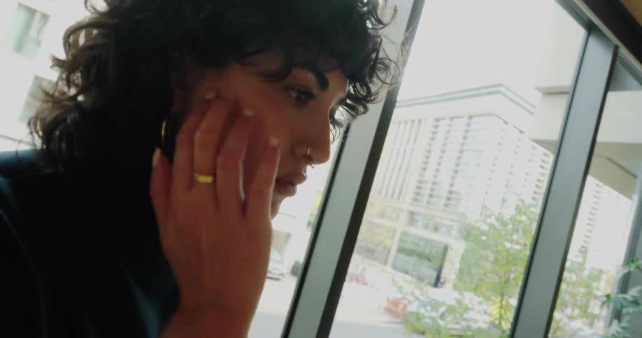 A woman types on her laptop near a large window in a modern office on a bright day