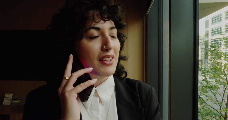 Professional on a phone call near the window in a welllit meeting room