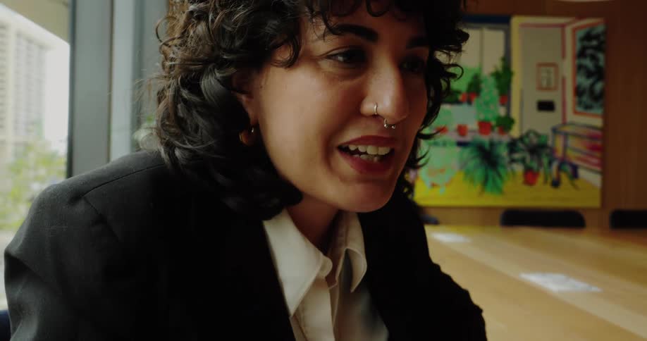 Woman seated at a table smiles while gesturing with a pen in a colorful meeting space