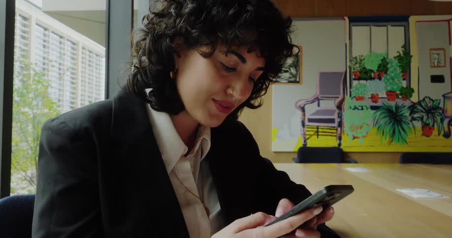 A woman is engrossed in texting on her smartphone while seated in a modern office