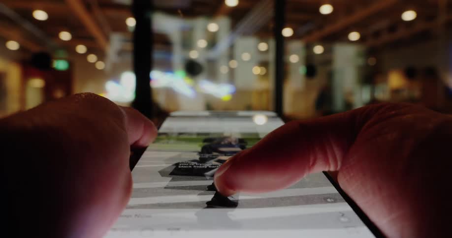 Closeup of hands scrolling a smartphone in warm blurry indoor light