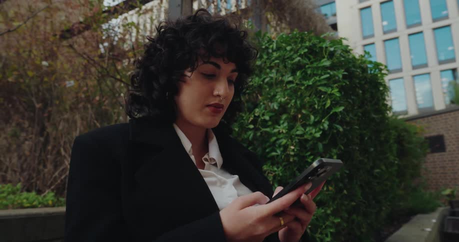 Woman stands outside of downtown buildings texting on her phone