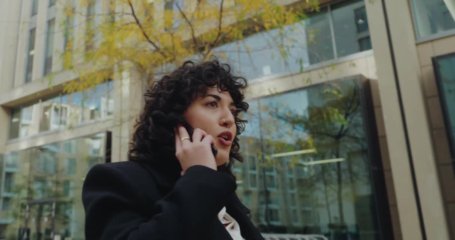 A woman with curly hair is walking down the street in a city talking on the phone