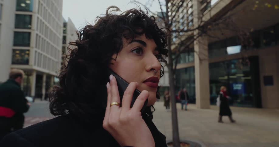 Woman walks along the sidewalk while talking on the phone in a busy urban area