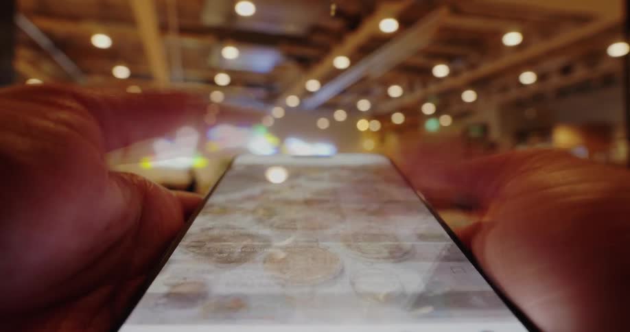A close view of hands quickly scrolling through text on a smartphone screen indoors with blurry lights in the background
