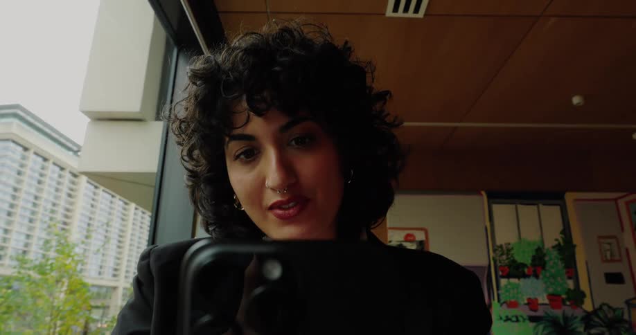 Woman smiles while holding a smartphone in a welllit indoor setting