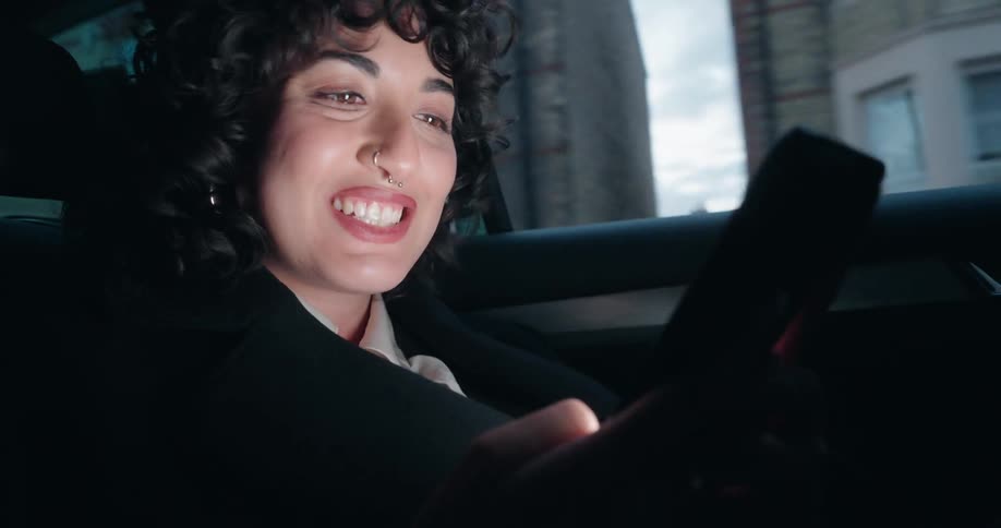 Woman inside the car looks at an illuminated smartphone while riding along the street