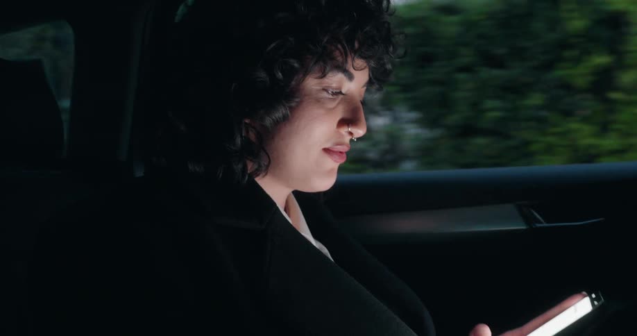 Woman looks at her phone screen while riding in the back seat of a car