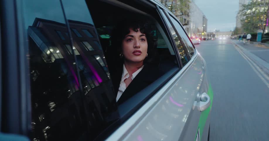 Woman looks out the open car window at the street while riding at dusk