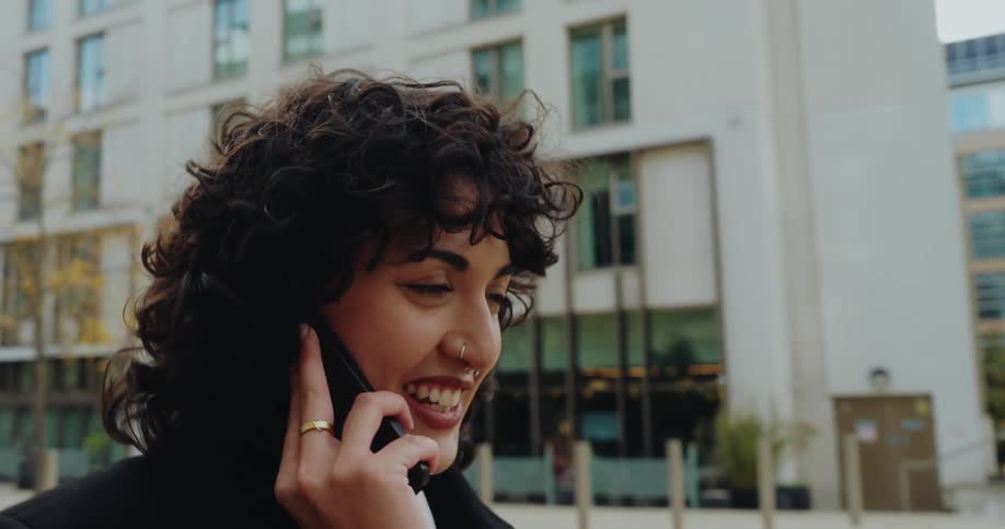 A female shown from the shoulders up is walking while talking on the phone in a city