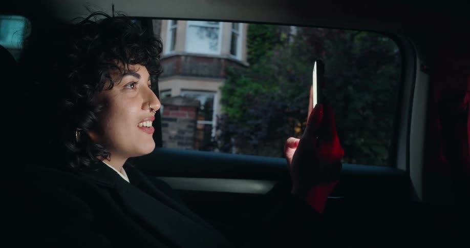 Person sitting in the back seat smiles while looking at a smartphone lit by its screen