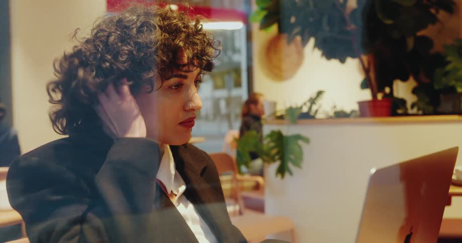 The face of a young woman who is using a laptop and placing her hand on her curly hair