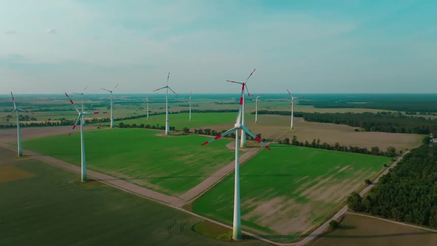 Aerial view of wind turbines stands across wide green fields under a partly cloudy sky