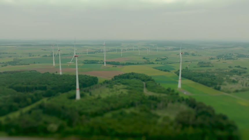 Aerial of multiple operating windmills in a green rural area during daytime