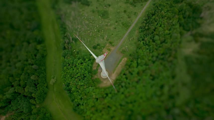 Aerial view of a wind turbine spinning over land with trees and vegetation
