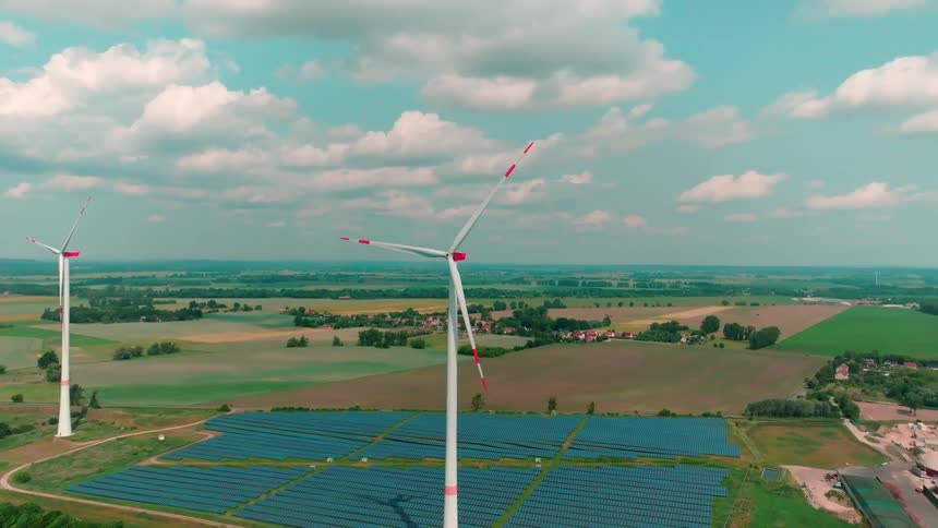 An aerial view of wind turbines overlooking a large solar panel array in a green rural landscape
