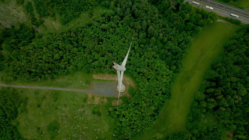 A large windmill is moving near a highway full of traffic