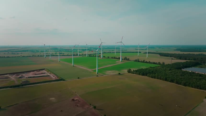 Aerial view of wind turbines over green farmland and forest under overcast sky