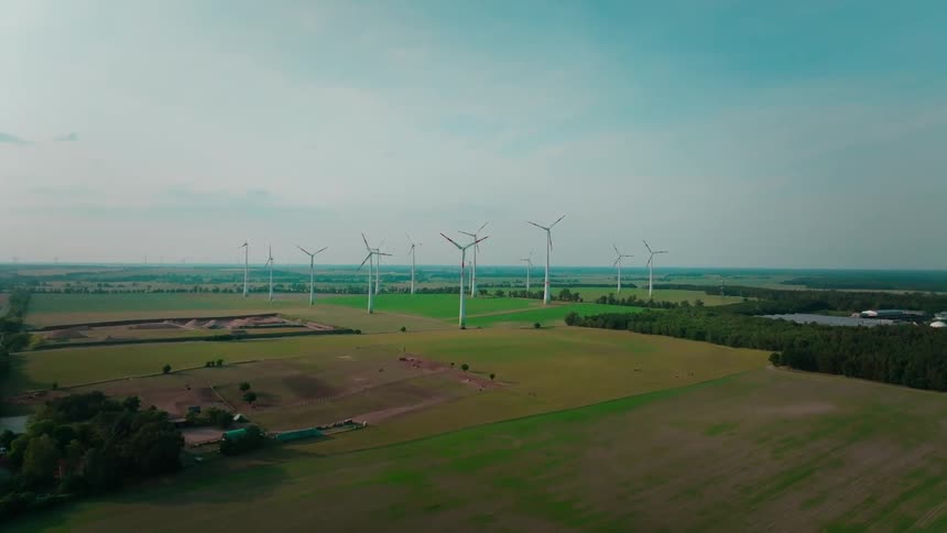 Wind turbines stand in a row across a wide green rural landscape