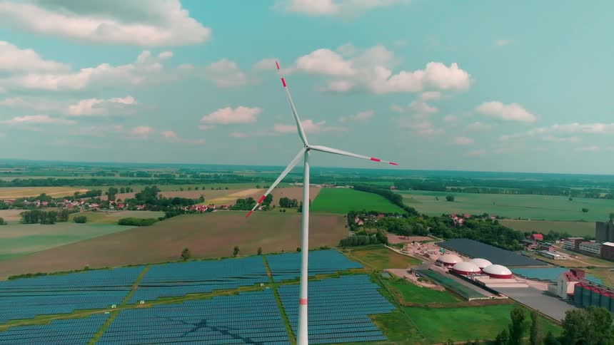 Wind turbine spins above wide fields with solar panels surrounding it