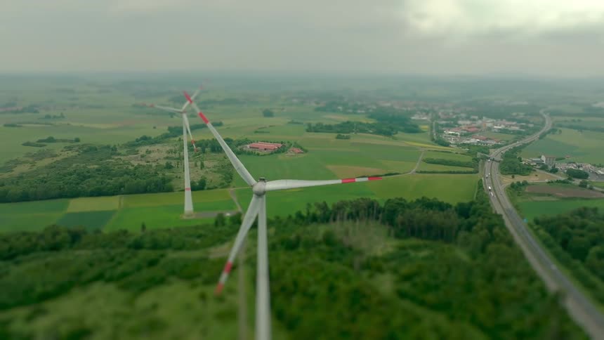 Wind turbines spin above a vast rural landscape seen from above
