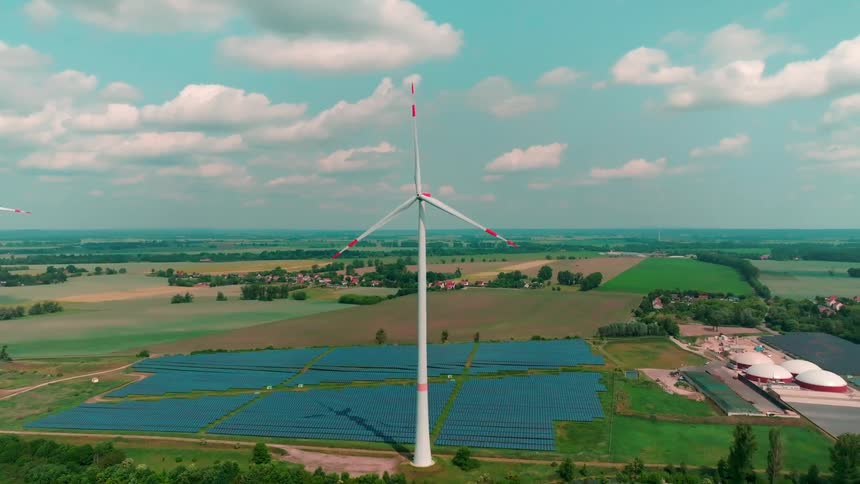 Aerial of operating windmills and panels at a power plant in a rural area during daytime