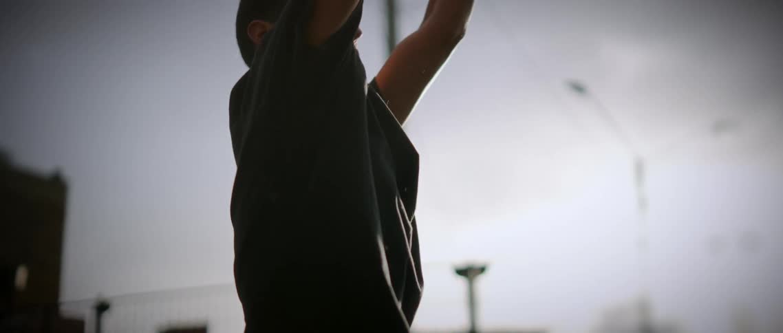 The video displays a young man in profile view silhouetted against a bright overcast skyhe is shown holding a darkcolored ball lifting it high above his head with both arms before bringing it back down