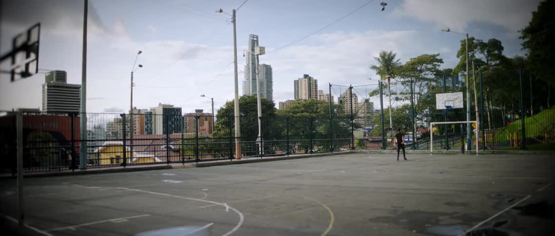 Person plays basketball alone on an outdoor court with buildings in the background