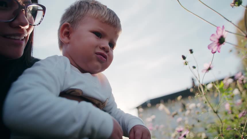 Mother and son reach out to flowers in a garden on a sunny day