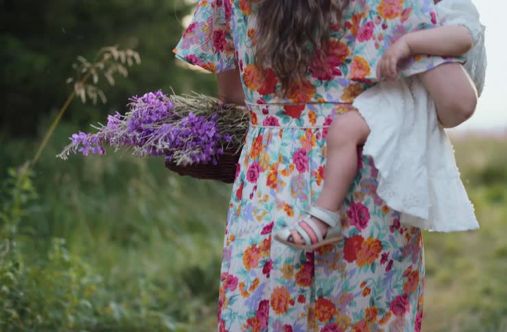 Woman carrying a child while holding a bouquet of purple flowers