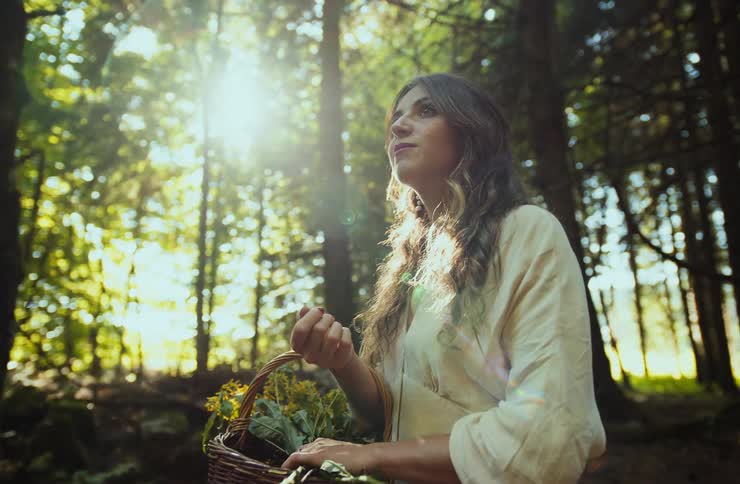 A young indian woman stands in the forest at midday holding a basket filled with flower plants