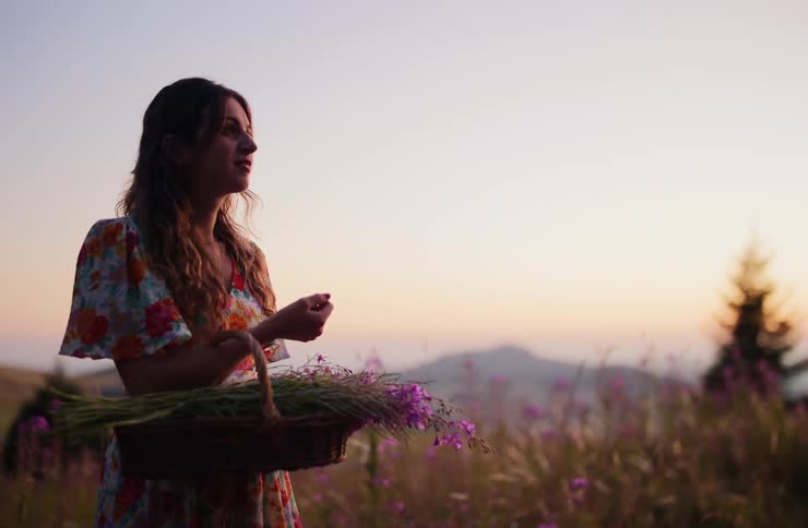 Woman holding a basket with purple flowers in a field at sunset