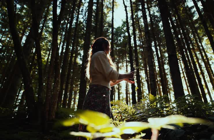 Woman leaning down to pick a leaf in a sunlit forest