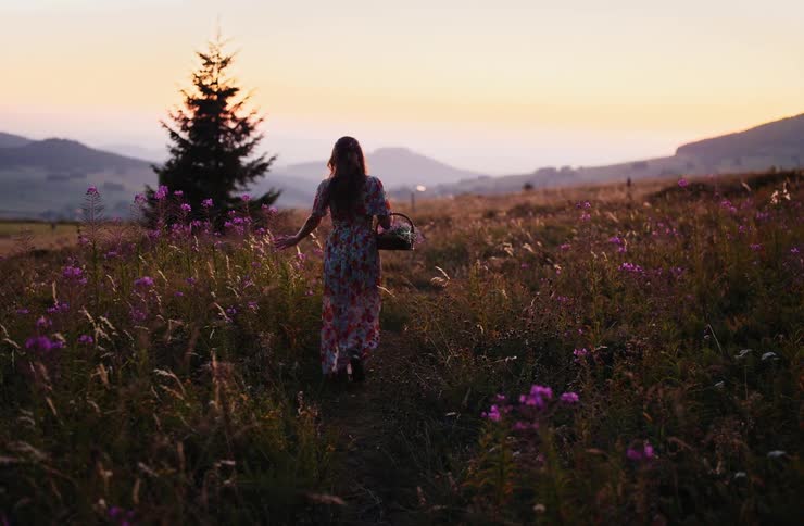 Woman walking through a field with purple flowers at sunset