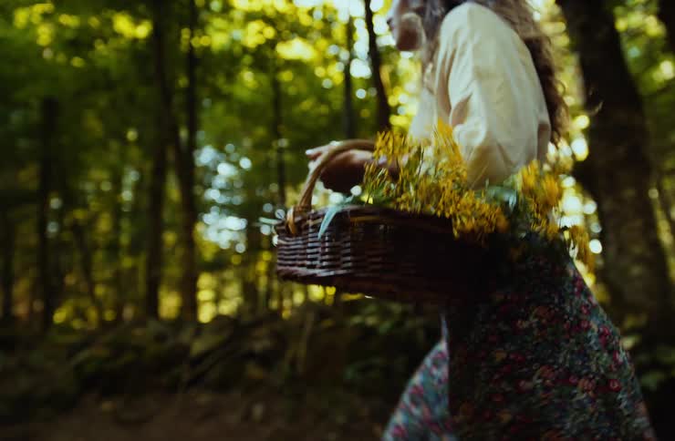 Woman walking through the forest carrying a basket filled with yellow flowers