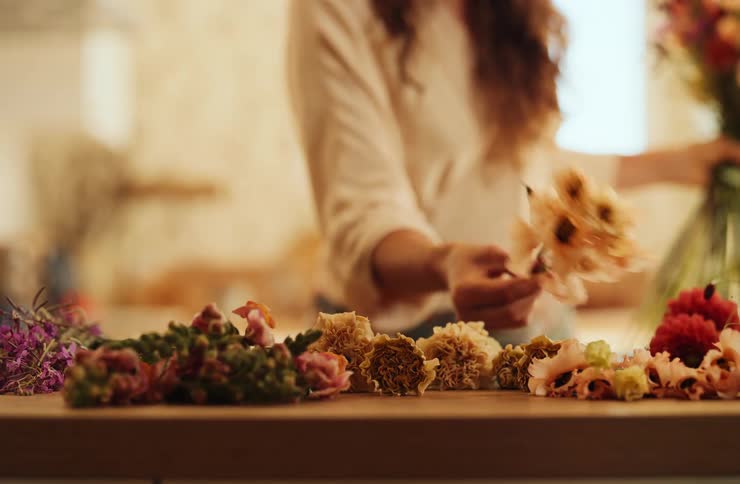 Flowers grouped on wood as woman arranges bouquet in the background