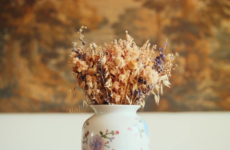Closeup of a porcelain vase holding dried flowers on a table