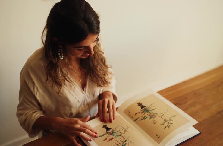 Woman observes botanical illustration with green leaves and red berries on wooden table