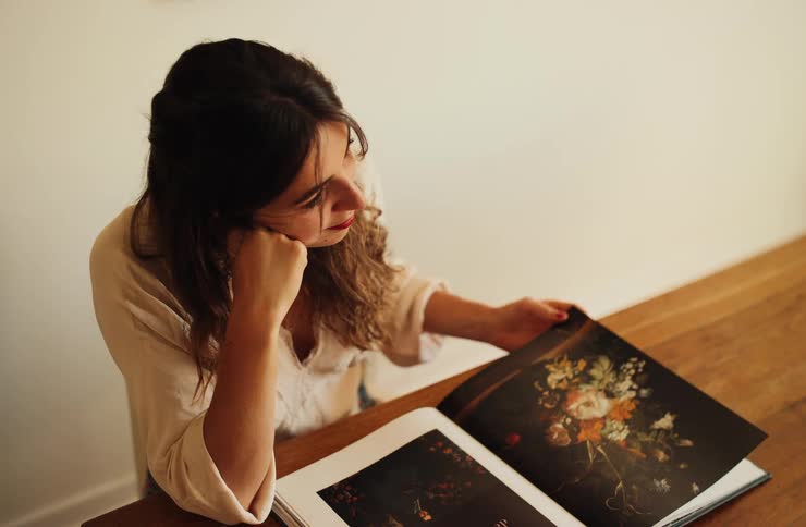 Woman flips through illustrated book with colorful figures on wooden table