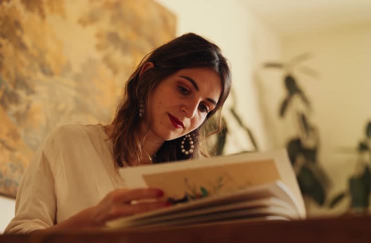 Woman observes printed page in front of abstract painting and indoor plants