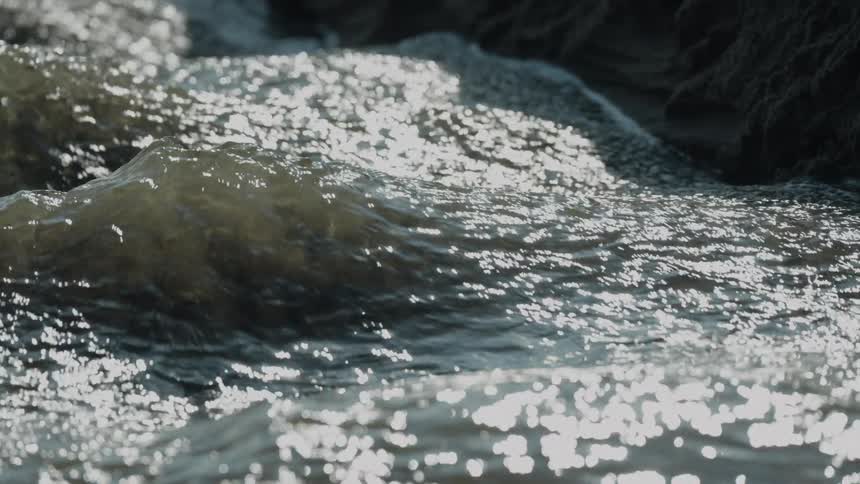 Current reflects sunlight between dark rocks in natural setting
