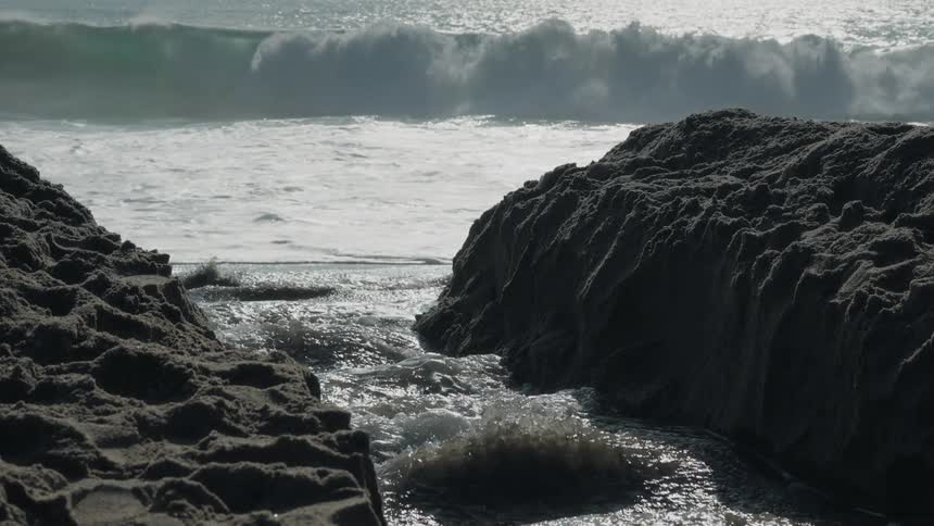 Water flows between rocks along the coast as waves roll in to shore
