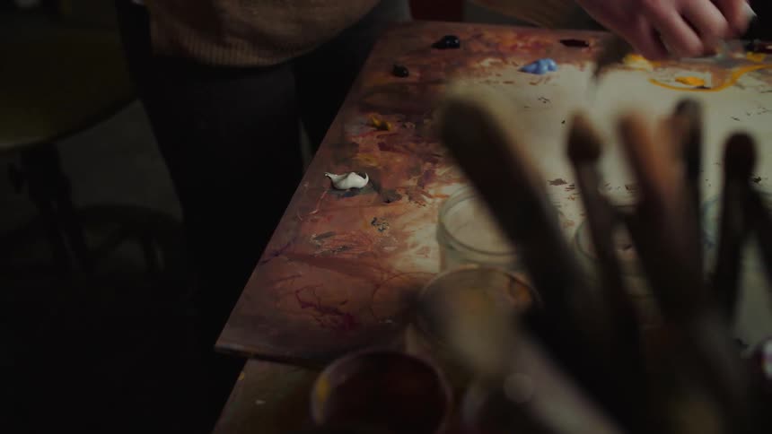 Hands wiping paint on a painting table filled with art materials