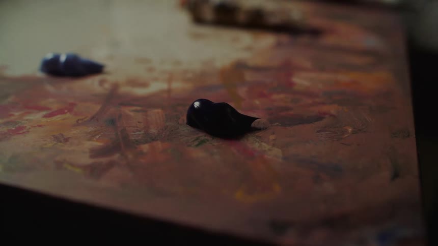 Hand squeezes dark blue paint onto palette already marked by varied tones and brush strokes
