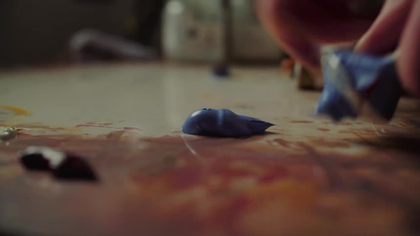 Blue paint being squeezed onto surface with traces of other colors in artistic setting