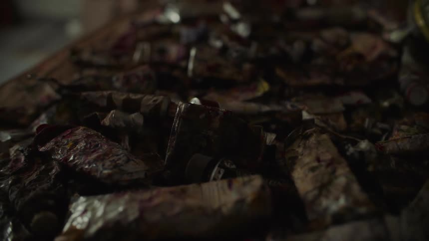 Crumpled paint tube reveals traces of vibrant colors on workbench in artistic setting