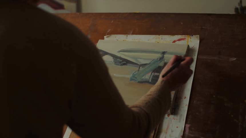 Closeup of an artists hand painting on a small canvas on a wooden table